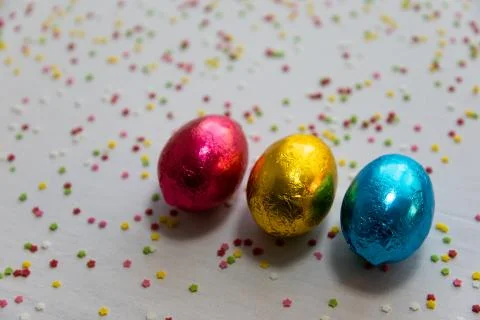 Three colored chocolate easter eggs on white background and colorful confetti Stock Photos