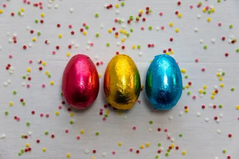 Three colored chocolate easter eggs on white background and colorful confetti Stock Photos