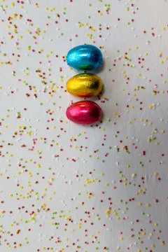 Three colored chocolate easter eggs on white background and colorful confetti Stock Photos