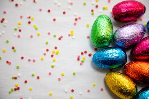 Three colored chocolate easter eggs on white background and colorful confetti Stock Photos