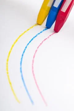 Three colored crayon sticks draw lines forming a curve on white paper Foto stock