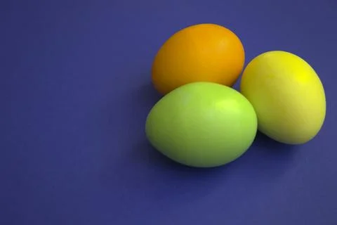 Three colored eggs lie on a purple background. Stock Photos