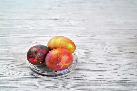 Three colored eggs in a transparent saucer on a light natural background Stock Photos