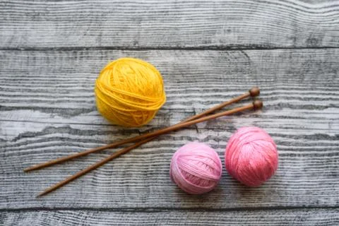 Three colored wool balls, knitting needles on the wooden background. Stock Photos