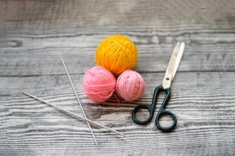 Three colored wool balls, knitting needles and scissors on the wooden backgro Stock Photos