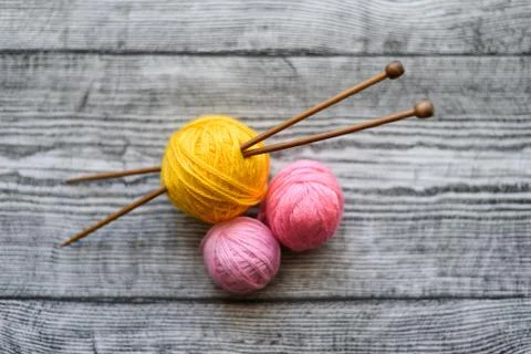 Three colored wool balls, knitting needles on the wooden background. Stock Photos