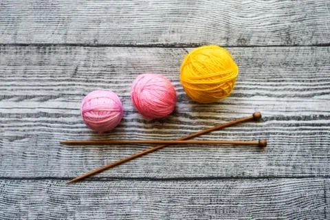 Three colored wool balls, knitting needles on the wooden background. Stock Photos