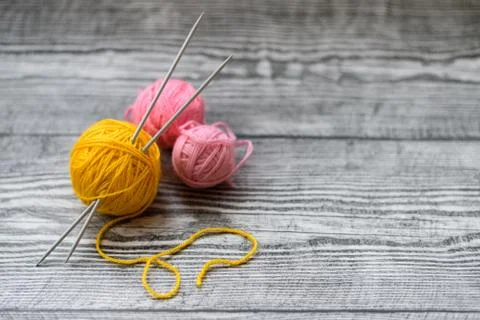 Three colored wool balls, knitting needles on the wooden background. Stock Photos
