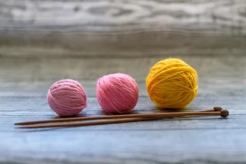 Three colored wool balls, knitting needles on the wooden background. Stock Photos