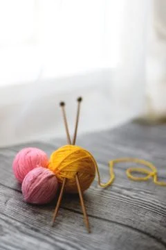 Three colored wool balls, knitting needles on the wooden background. Stock Photos