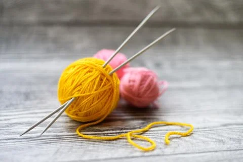 Three colored wool balls, knitting needles on the wooden background. Stock Photos