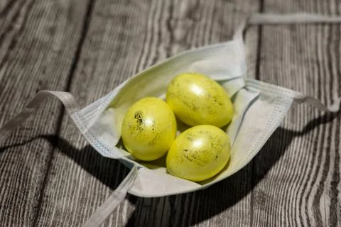 Three colored yellow easter eggs laying in medical mask. Stock Photos