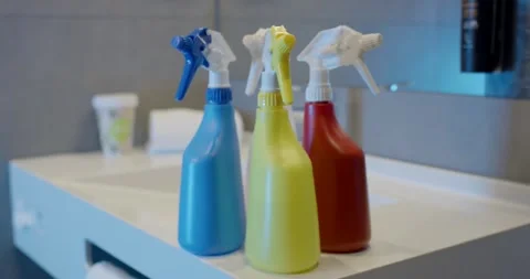 Three Colorful Cleaning Spray Bottles in a Row on White Shelf Stock Footage 340272952