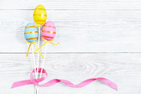 Three colorful Easter egg with pink ribbon bow on blue old wooden table. Stock Photos