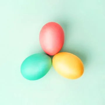 Three colorful Easter eggs in triangle on mint colored background. Flat lay. Stock Photos