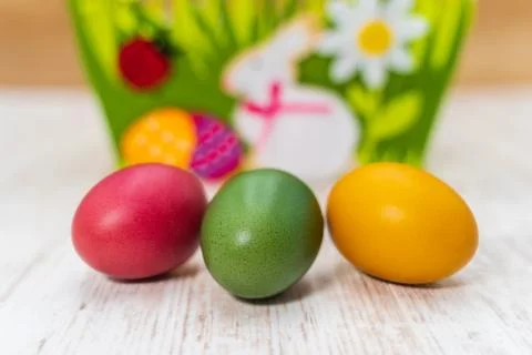 Three colourful Easter eggs in front of felt Easter basket with wooden backgr Foto stock