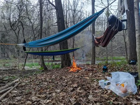 Three colourful hammocks hang from trees with a campfire in the middle Stock Photos