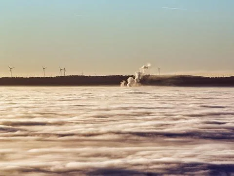 Three columns of steam rising from cloud cover wind turbines wind power station Stock Photos