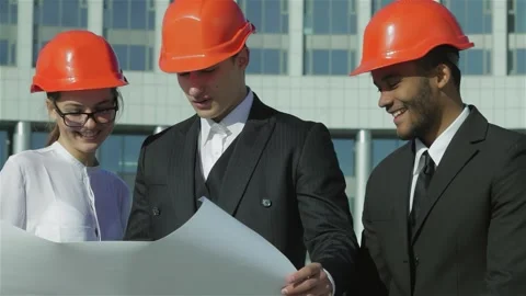 Three confident engineers in protective helmets reviewing blueprints Stock Footage 311933633
