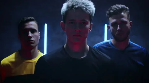 Three confident young men stand in a dark studio against a black background with 库存影片 157102136