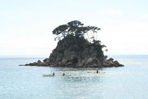 Three conoes pasing along in front of a rocky island Stockfoto's