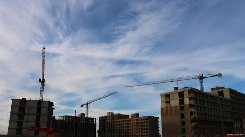 Three construction cranes are behind houses against the sky Stock Photos