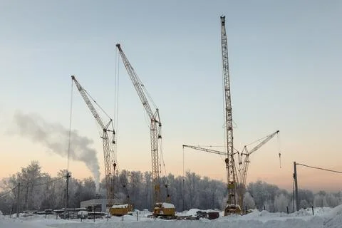 Three construction cranes in cold winter against the background of frozen tre Stock Photos