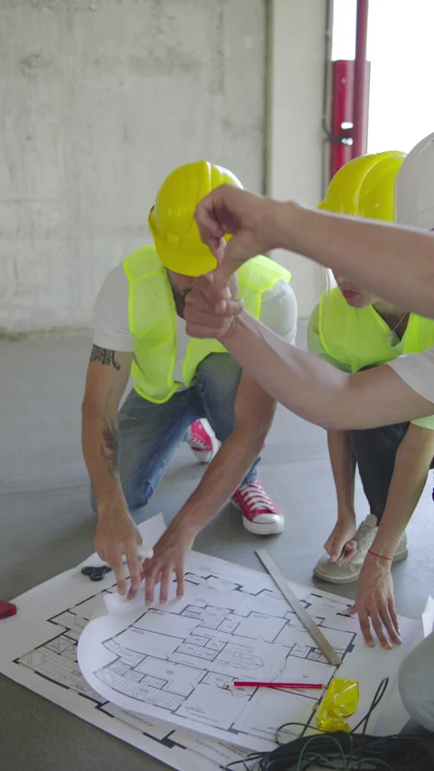 Three Construction engineers in safety helmets inspect wiring plans at a Vídeo Stock 348247578