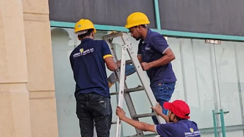 Three construction workers, two on a ladder and one spotting, wearing hard hats Stock Footage 311589441