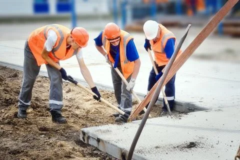 Three construction workers in vests and hard hats lay concrete slab at Stock Photos