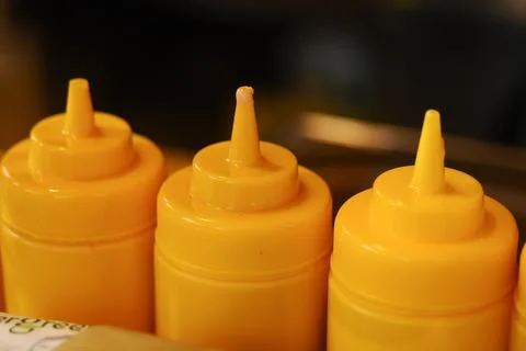 Three containers hold yellow condiment on a table Stock Photos
