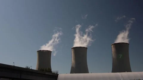 Three cooling towers release white steam against clear blue sky symbolizing ener Stock Footage 314823364