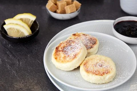 Three cottage cheese pancakes with jam lie on a gray plate Stock Photos