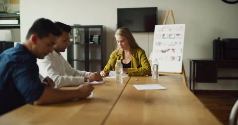 Three coworkers go over notes at meeting at wood desk in modern office during th Stock Footage 199460532