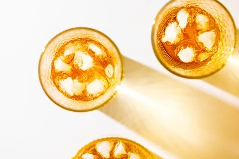 Three cropped glasses of iced apple juice with long golden shadows on white.. Stock Photos