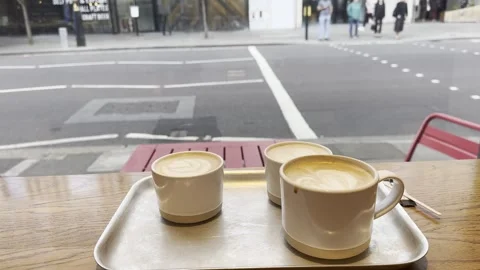 Three cups of coffee on tray by window with london street traffic background Stock Footage 336680039