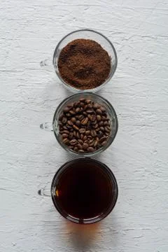 Three cups of ground coffee, coffee beans and brewed coffee in one row Stock Photos