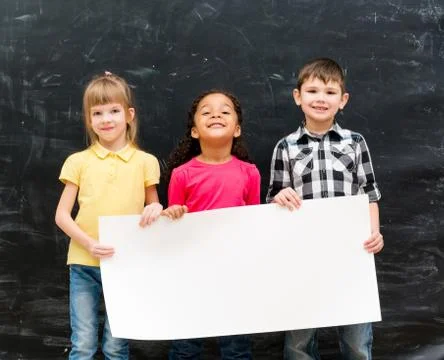 Three cute children holding an empty paper sheet for ad Foto stock
