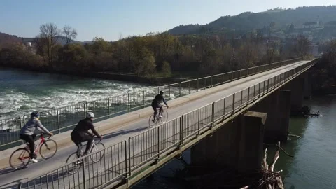 Three cyclists ride across the bridge over rough river Stock Footage 143362144