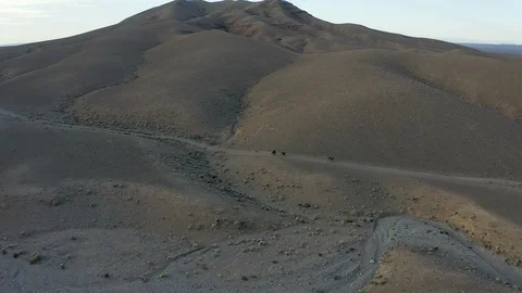 Three cyclists ride uphill through a stark and desolate rocky desert. Stock Footage 127013644
