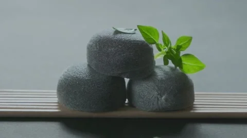 Three dark Daifuku moti dessert on bamboo mat. Green leaves fall on top. Slow Stock Footage 178489814