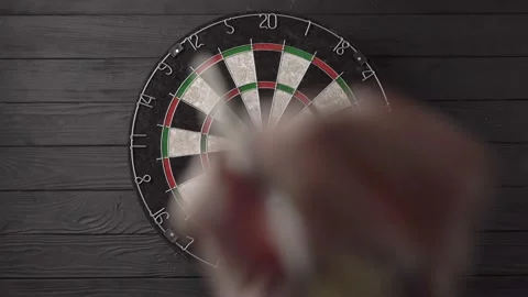 Three darts are aimed and thrown by hand and hit the dartboard on a black wooden Stock Footage 237873293