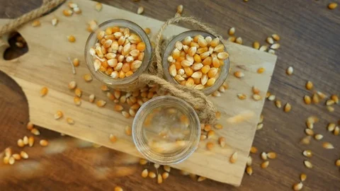 Three decorative glass cups full with corn, corn falling, wooden background 스톡 동영상 124205866