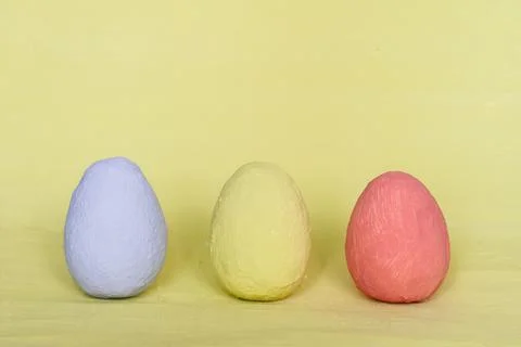 Three decorative multi-colored eggs on a pastel yellow background. Stock Photos