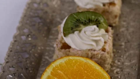 Three delicate bite-sized square cake pieces topped with whipped cream Video stock 308923220