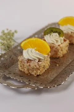 Three delicate bite-sized square cake pieces topped with whipped cream Stock Photos