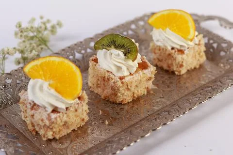 Three delicate bite-sized square cake pieces topped with whipped cream Stock Photos