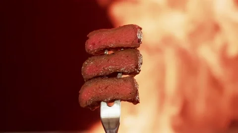 Three delicious pieces of medium-rare beef steak are held on a fork on a black Stock Footage 156654742