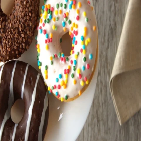 Three delicious sweet donuts rotating on a plate. Rustic wooden table. Looped Stock Footage 69674297