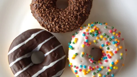 Three delicious sweet donuts rotating on a white plate. Looped Stock-Footage 69984412